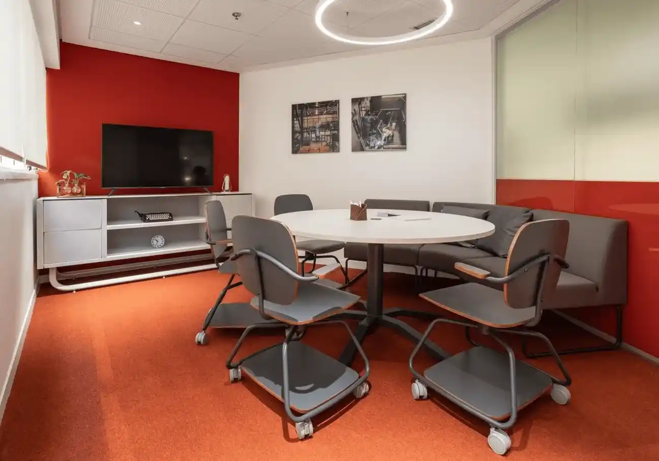 
Sala de reuniões moderna e colorida com paredes brancas e vermelhas, poltronas confortáveis, mesas e uma televisão grande.