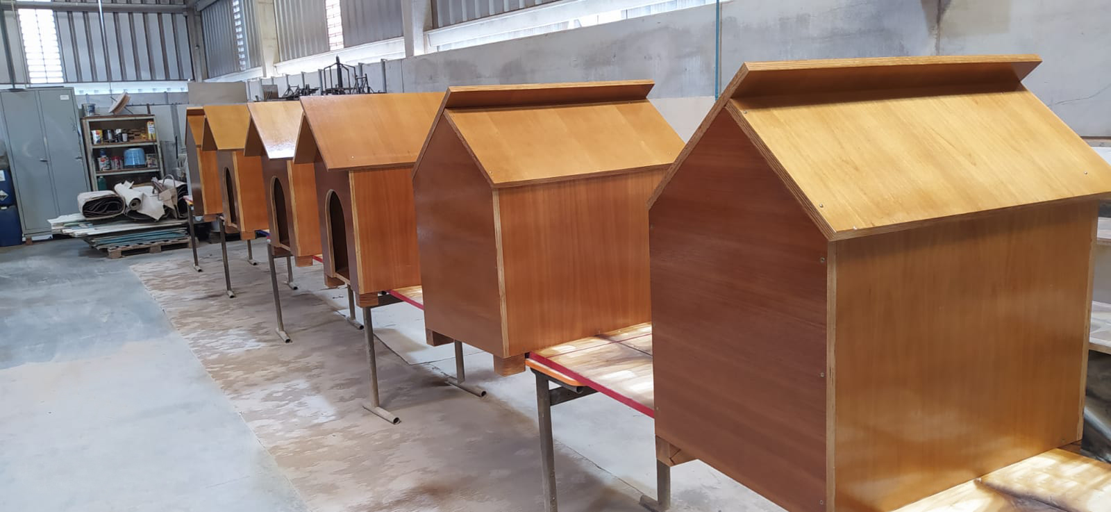 casas para cachorros feitas de madeira de reaproveitamento organizadas em fileira em cima de uma mesa de trabalho na fábrica