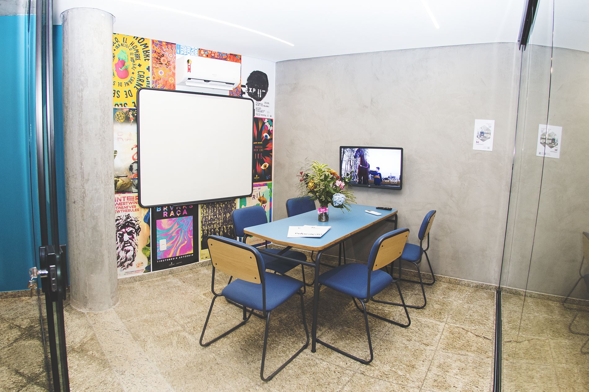 Sala de reunião dentro do coworking Escola Portal, com mesa e cadeiras, parede decorada com postes e lousa branca fixada sobre ela