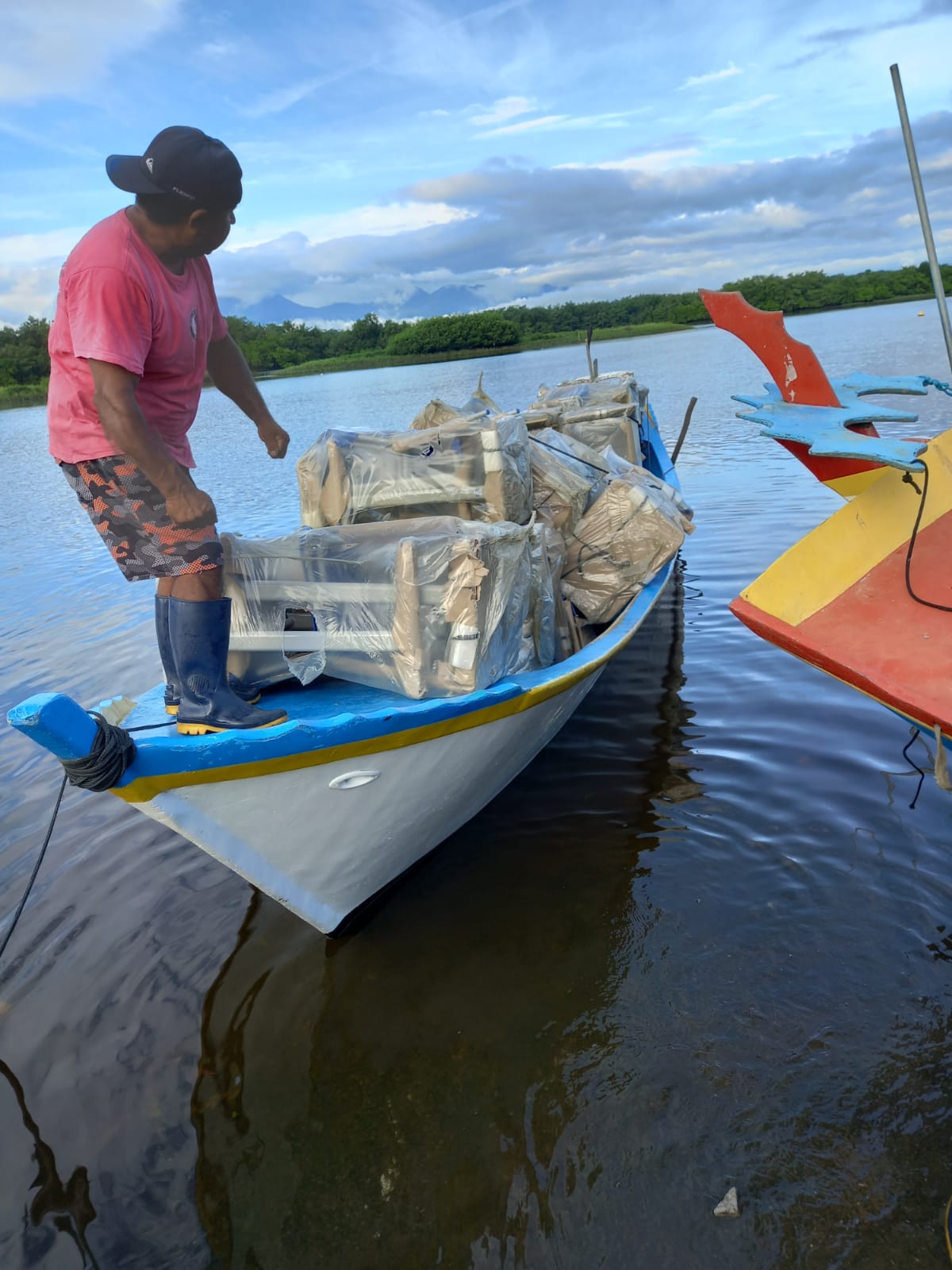 Homem conduzindo pequeno barco com móveis escolares embalados sobre ele