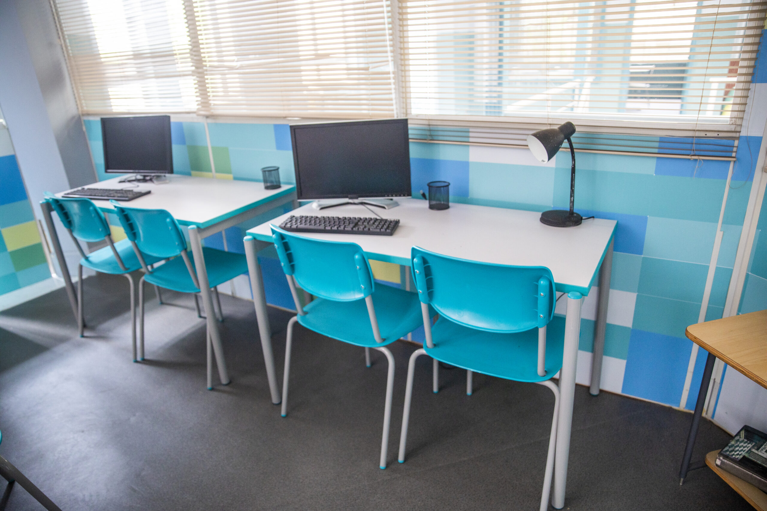 Laboratório de informática com mesas e cadeiras cor azul, sobre as mesas computadores e equipamentos eletronicos
