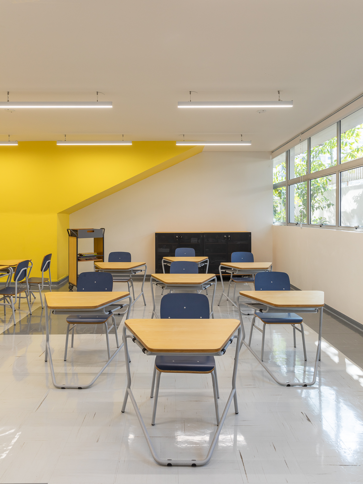 Sala de aula com carteiras de tampo trapezoidal e cadeiras organizados em fileiras