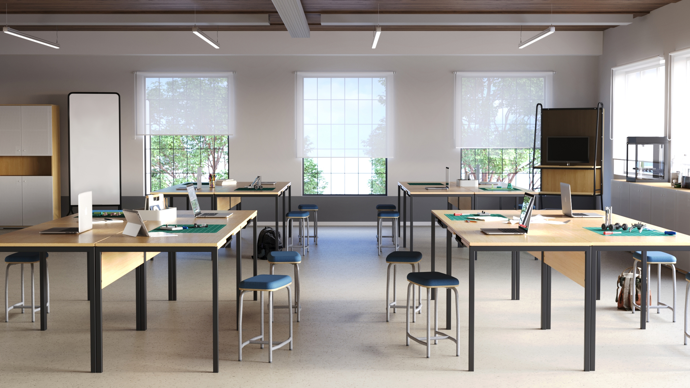 Sala de aula com mesas e bancos individuais, ao fundo três janelas grandes . Sobre as mesas equipamentos e ferramentas par construção de protótipos eletrônicos.