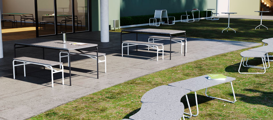 pátio externo com assentos coletivos em formação, gramado e com árvores ao fundo criando sombras no ambiente. A direita duas mesas com bancos coletivos.