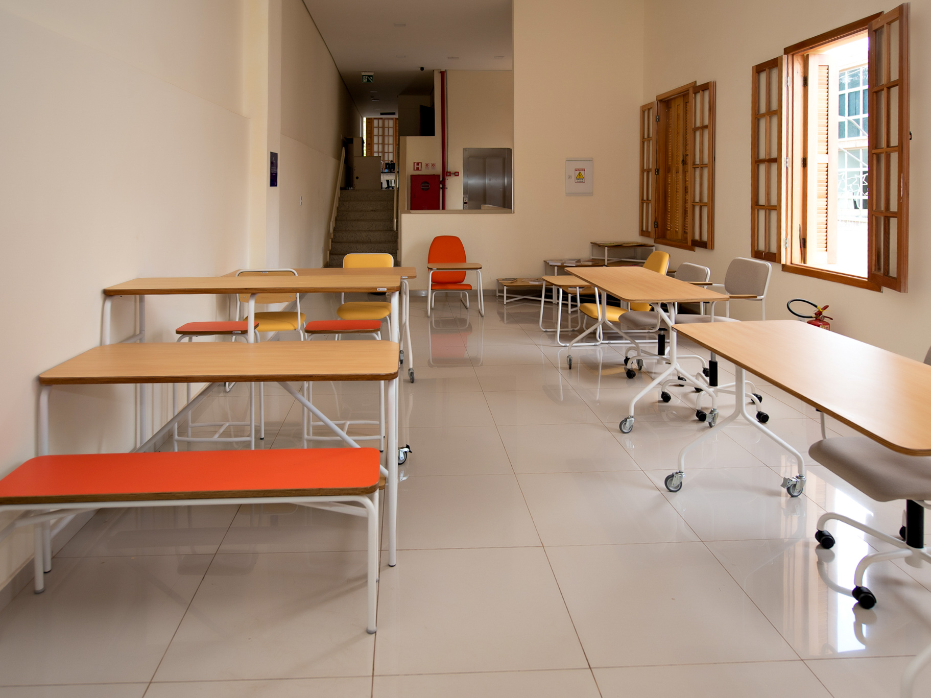 Sala de uma biblioteca com mesas e bancos coloridos.