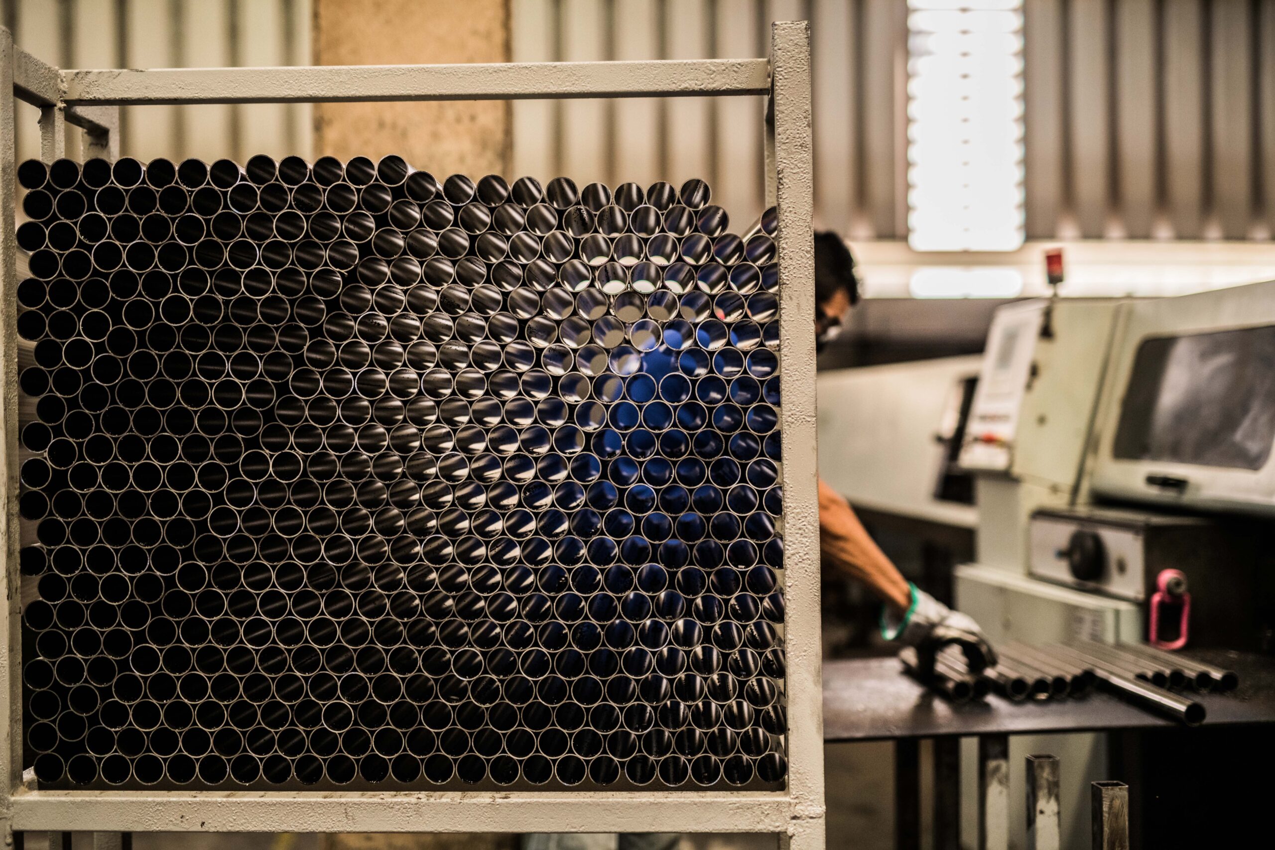 Imagem de um trabalhador em uma fábrica, organizando tubos metálicos.