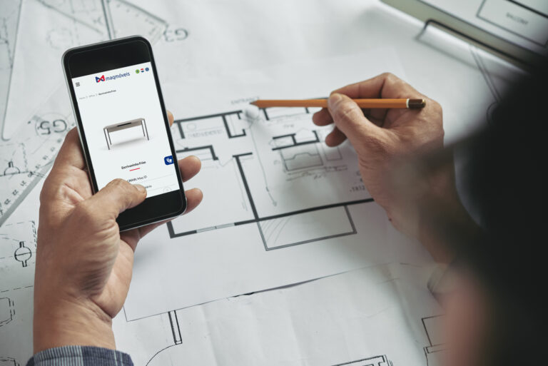 Mãos segurando um smartphone com um site de móveis e um lápis sobre uma planta baixa, planejando um ambiente.