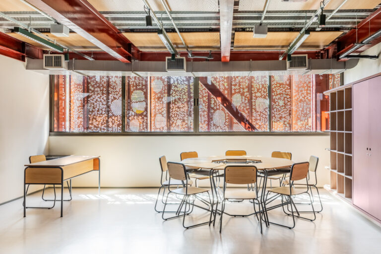 Sala moderna com mesas circulares, cadeiras escolares e estante, destacando a presença da Maqmóveis no anuário da Revista Projeto.